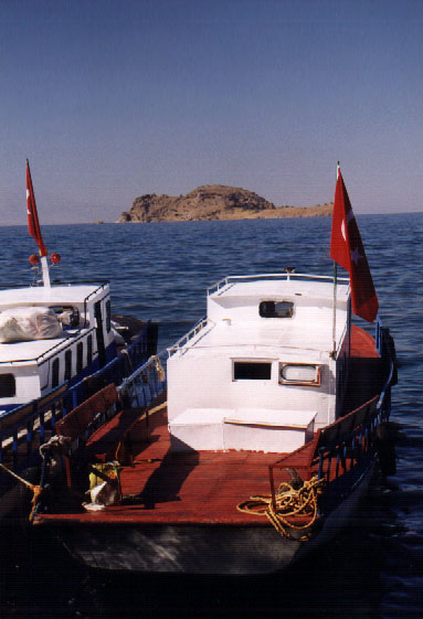 A boat is docked on shore across from Akdamar Island