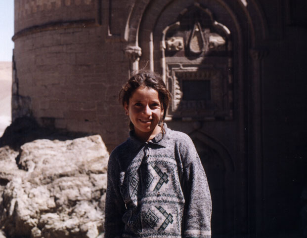 young girl in sweater poses in front of a castle wall